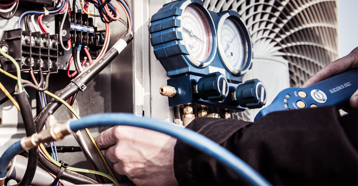 Hands with tools working on an air conditioning unit showing pressure valuves and wiring